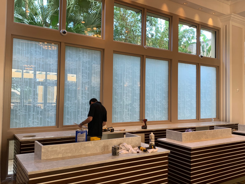 Technician installing privacy window films behind reservation desk at Hyatt Coconut Point.